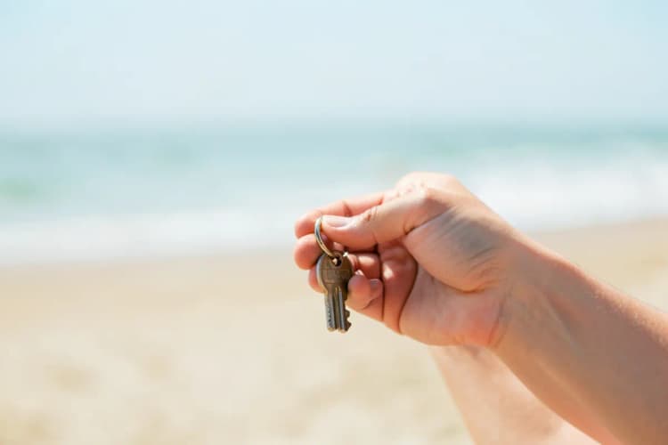 Mãos segurando uma chave de casa com uma praia desfocada ao fundo
