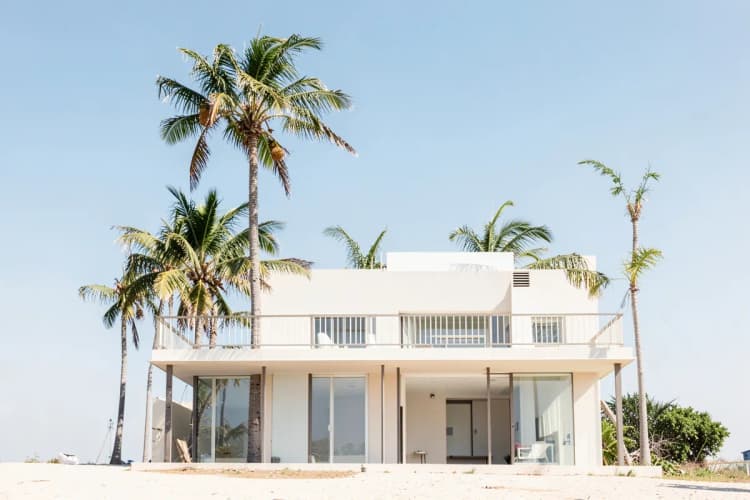 Fachada de uma casa de praia com varanda e coqueiros