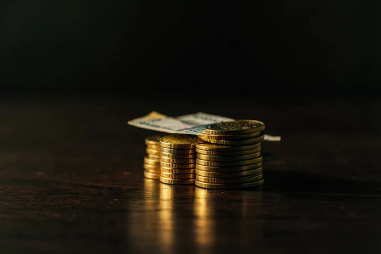 Moedas de ouro e notas de dinheiro empilhadas sobre uma mesa de madeira escura